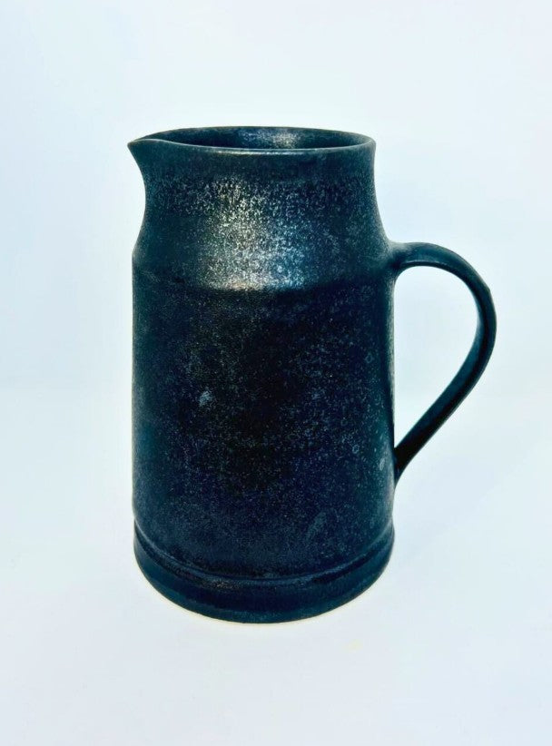 A dark, speckled black ceramic pitcher with a handle and spout, photographed against a plain white background.