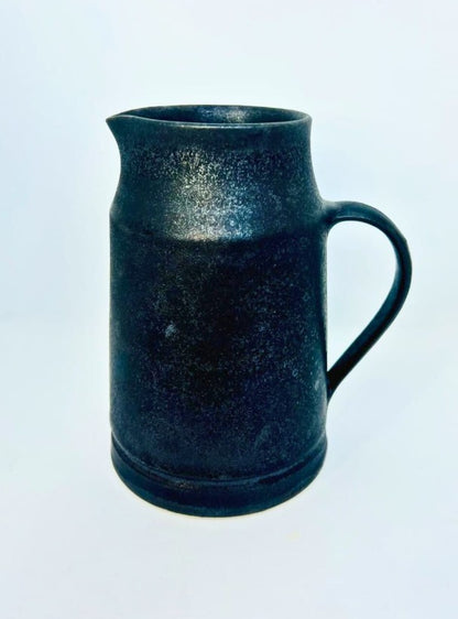 A dark, speckled black ceramic pitcher with a handle and spout, photographed against a plain white background.