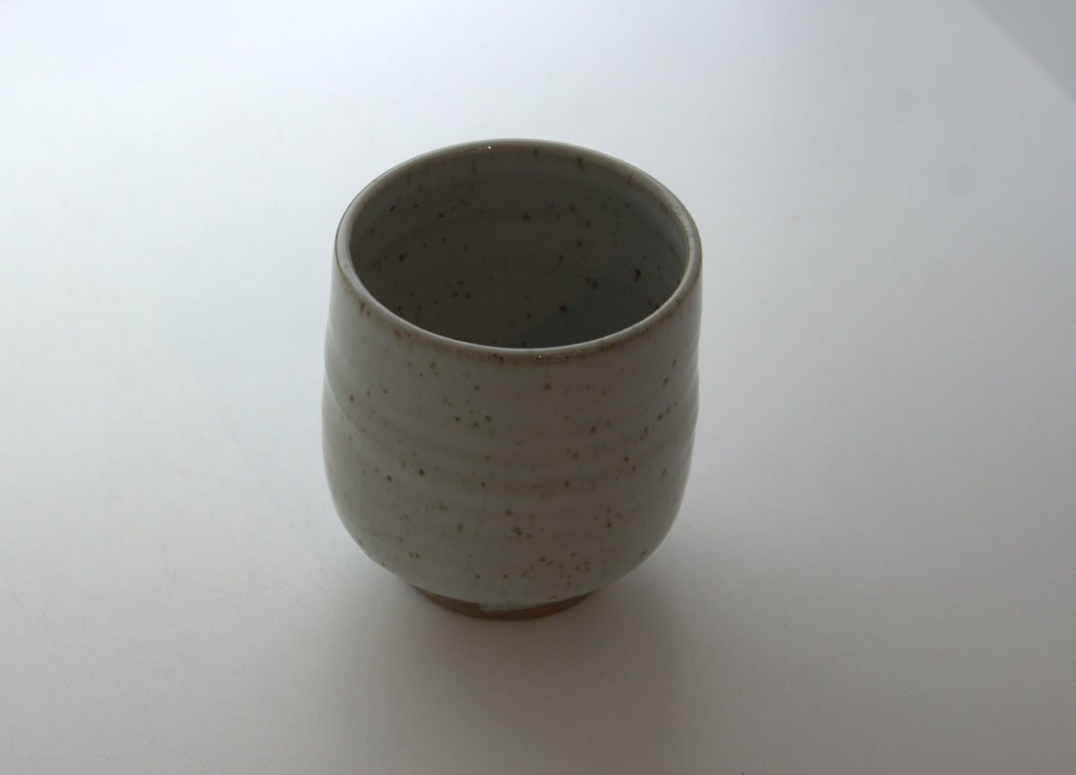 A handmade ceramic tea cup with a textured, speckled glaze in a light grayish-beige color, shown on a plain white background.