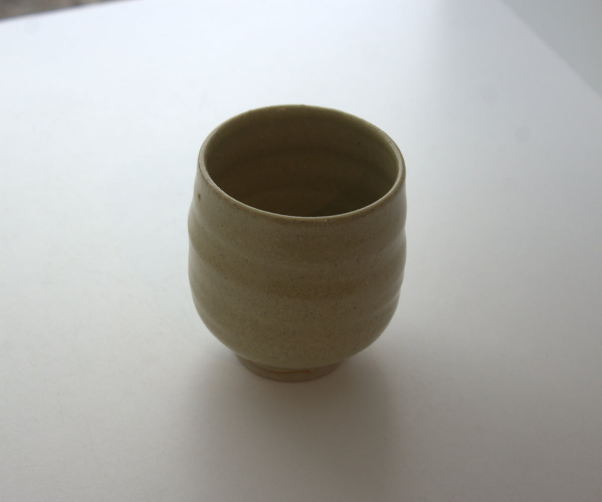 A small handmade ceramic cup with a textured, ribbed exterior and a smooth, matte finish, shown on a plain white surface.