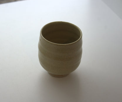 A small handmade ceramic cup with a textured, ribbed exterior and a smooth, matte finish, shown on a plain white surface.