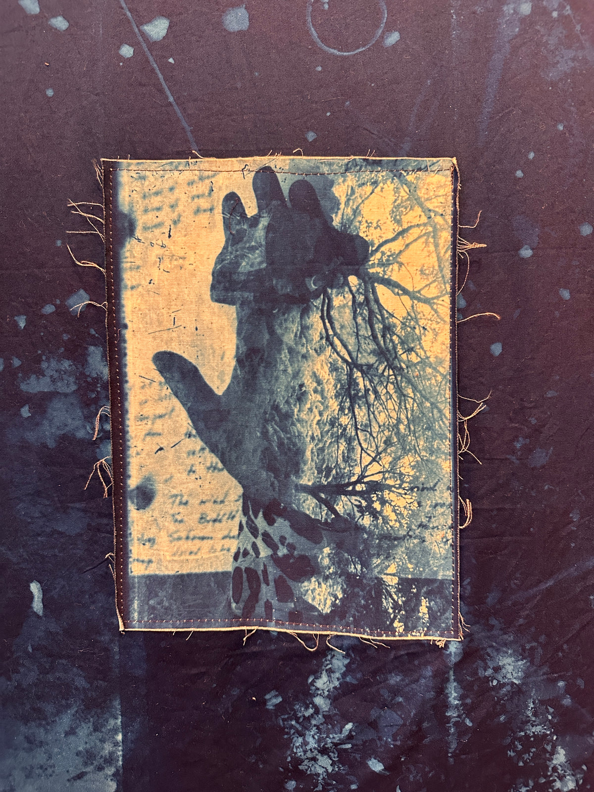 A rectangular fabric patch with a distressed graphic of a hand reaching upward toward tree roots, set against a dark textured background.